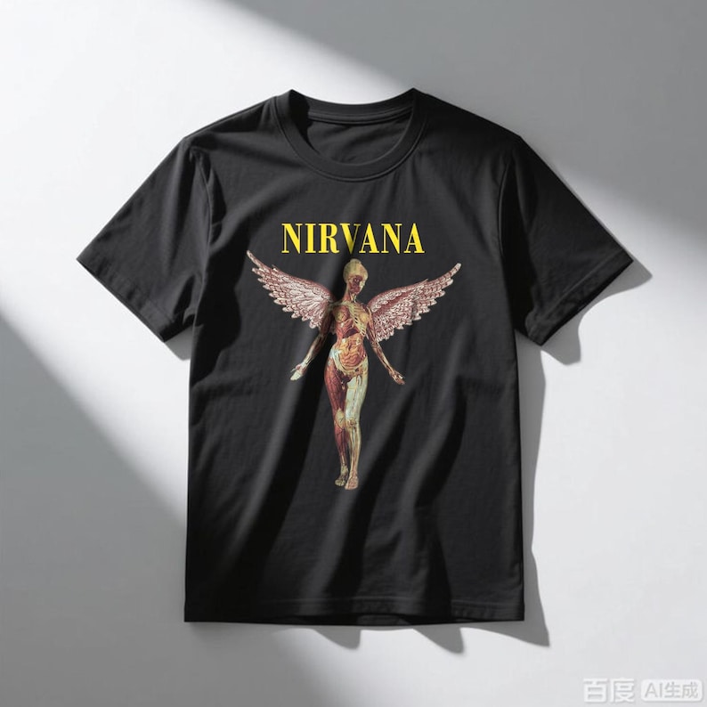 May include: Black t-shirt featuring the word "NIRVANA" in yellow block letters above a graphic of a nude figure with angel wings. The figure is in a standing pose with arms outstretched. The shirt is made of a soft material.