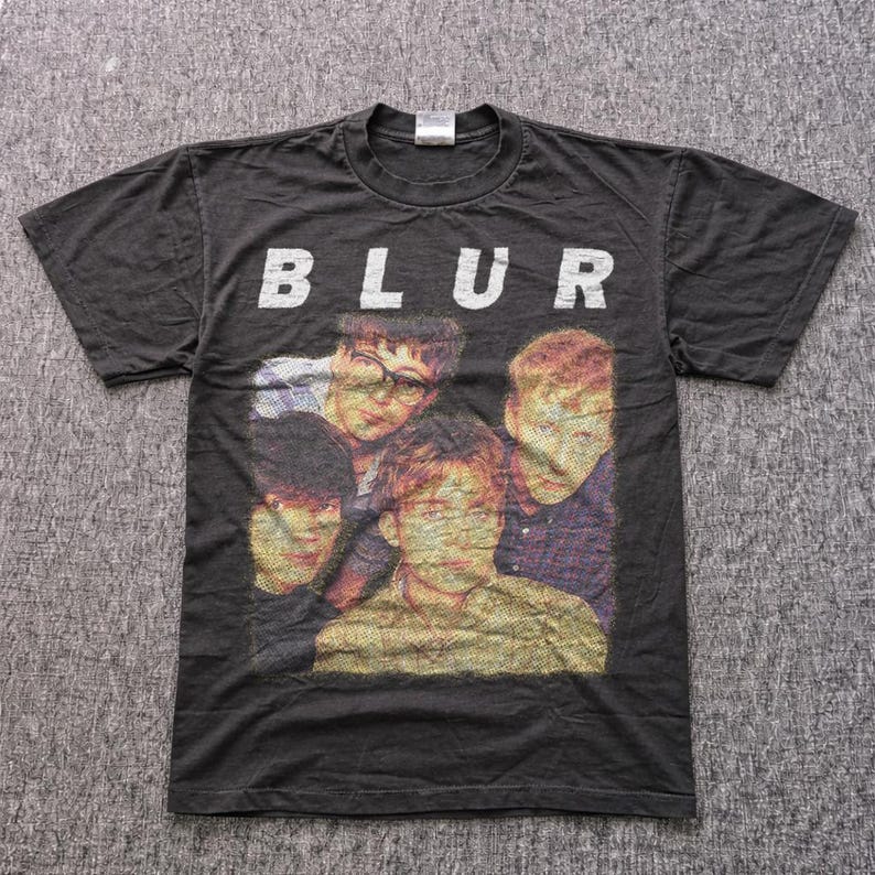 Puede incluir: Camiseta negra con el nombre de la banda Blur en letras blancas sobre una foto de los miembros de la banda. La camiseta es de cuello redondo y parece ser de algod&oacute;n. Art&iacute;culo de m&uacute;sica vintage.