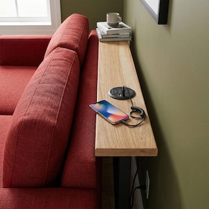 May include: A red sectional sofa with a wooden side table. A black power outlet with two plugs and a charging phone are on the table. A mug and books are stacked on the table. The wall is painted a light green.