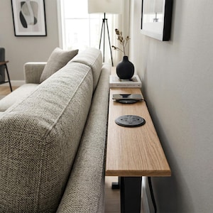 May include: A light wood side table with a built-in power outlet and USB ports, positioned next to a gray upholstered sofa. A black vase with dried stems and a book titled "Modern Design" are on the table. A wireless charging pad is also visible.