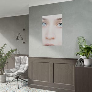 a modern living room with a large wall-mounted portrait of a woman's face, a white chair, a potted plant, and a wooden cabinet.