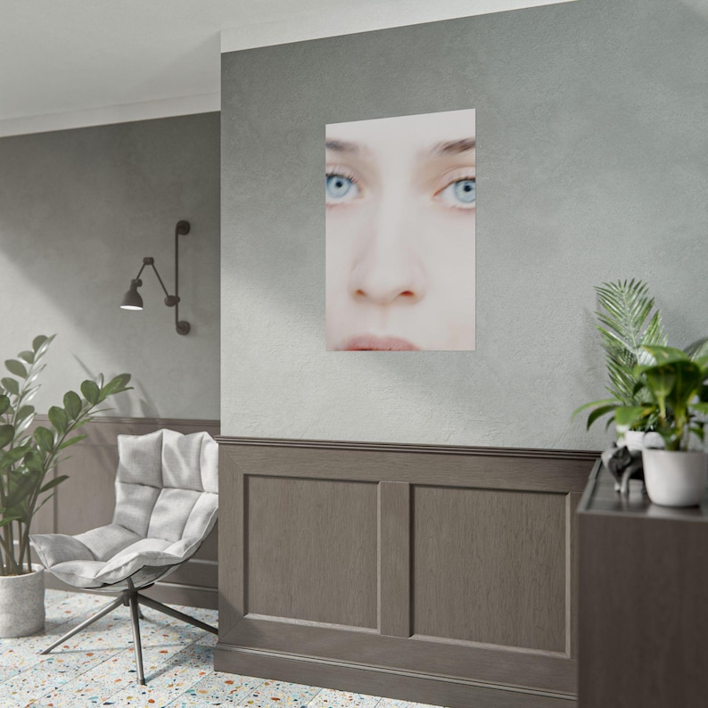 a modern living room with a large wall-mounted portrait of a woman's face, a white chair, a potted plant, and a wooden cabinet.
