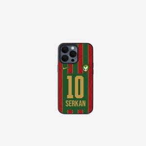 Könnte beinhalten: Handyhülle mit grün-rotem Streifenmuster, das an ein Fußballtrikot erinnert. Die Nummer "10" und der Name "SERKAN" sind in Gold dargestellt. Ein kleines Logo ist oben rechts sichtbar.