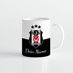 Könnte beinhalten: Weißer Keramikbecher mit schwarz-weißem Design. Der Becher zeigt ein Teamwappen mit Sternen, die Buchstaben "BJK", einen Halbmond und Stern und das Jahr "1903". Die Worte "Dein Name" sind auf dem Becher aufgedruckt.