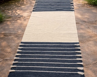 May include: A rectangular runner rug featuring a solid cream-colored center section flanked by two dark navy blue ends. The navy blue sections are decorated with horizontal white stripes and finished with small white tassels along the edges.