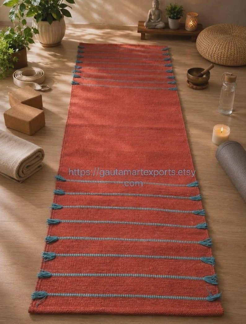 May include: A rectangular terracotta-colored woven runner rug featuring horizontal light blue stripes and decorative tassels along the side edges. The text https://gautamartexports.etsy.com is printed in the center of the rug surface.