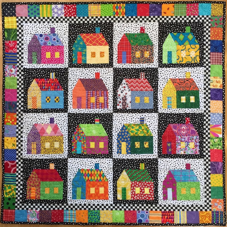 May include: A patchwork quilt with twelve house blocks, each a different colour and pattern, set against a black and white dotted background. The houses have chimneys and windows. The quilt has a black and white checkered border and a patterned edge.