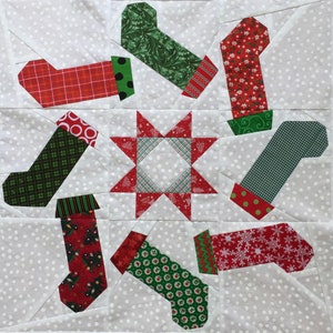 May include: A handmade Christmas quilt block featuring nine festive stockings in red and green patterns, including plaid, polka dots, and snowflakes. The stockings are arranged around a central red star on a white dotted background.