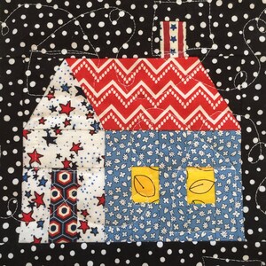 May include: A patchwork house design with a red and white zigzag roof, blue floral walls, and star-patterned sections. The house features yellow leaf-shaped windows and a star-striped chimney. The background is black with white polka dots.
