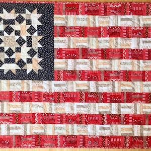 May include: A handmade American flag quilt featuring red, white and blue fabric. The stars are created using a star block pattern and the stripes are made with a patchwork design.
