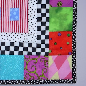 May include: A vibrant patchwork quilt with diverse patterns and colours. The quilt showcases squares of red and white stripes, polka dots, checkerboard, and floral designs. The border is black with white polka dots.