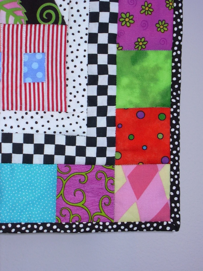 May include: A vibrant patchwork quilt with diverse patterns and colours. The quilt showcases squares of red and white stripes, polka dots, checkerboard, and floral designs. The border is black with white polka dots.