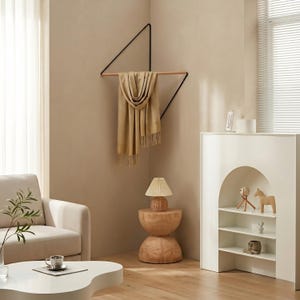 May include: A modern living room scene featuring a geometric wall-mounted scarf rack. The rack is black with a wooden bar, holding a beige scarf. A wooden side table with a lamp and a white cabinet with shelves are also visible.