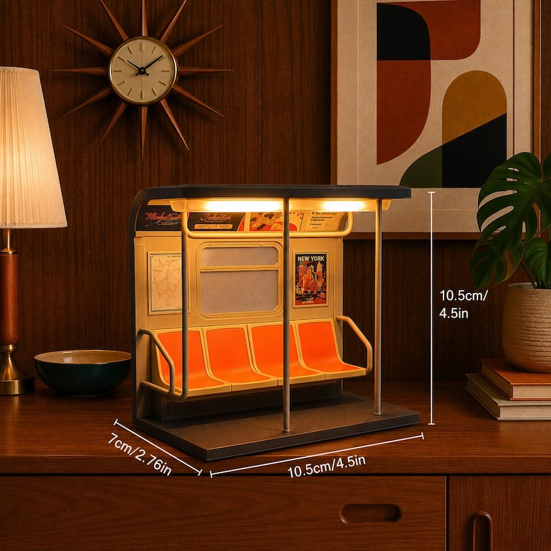 May include: A miniature subway car interior lamp featuring four orange seats, metal poles, and illuminated ceiling lights. The structure measures 4.5 inches in height, 4.5 inches in width, and 2.76 inches in depth, with visible New York signage.