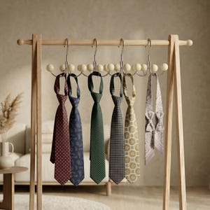 Puede incluir: Un perchero de madera exhibe una colección de corbatas estampadas. Las corbatas presentan varios diseños, incluyendo lunares, paisley y patrones geométricos, en colores como burdeos, azul marino y verde. También se incluye una pajarita lila claro.