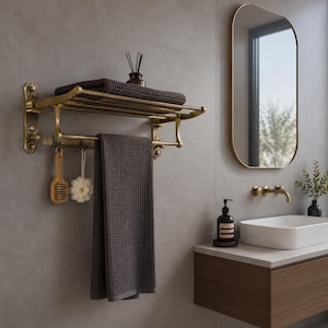 May include: A wall-mounted antique brass towel rack with a top shelf and a lower bar. The rack holds a folded dark grey waffle-weave towel on top and a hanging dark grey waffle-weave towel below, alongside a wooden brush and a white bath sponge.