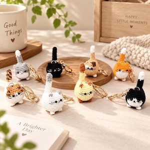 Può includere: Una collezione di otto piccoli portachiavi a forma di gatto realizzati all'uncinetto, di forma rotonda e in vari colori, tra cui nero, bianco, grigio, arancione e tartarugato. Ogni gatto ha una lunga coda dritta, dettagli ricamati e un anello dorato.