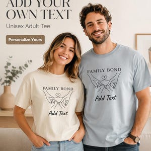 Può includere: Una t-shirt color crema e una t-shirt azzurra, entrambe caratterizzate da un disegno a linee nere di mani di adulti e neonati che si tengono per le dita con un cuore sopra, e il testo "FAMILY BOND" e "Add Text" stampato sul davanti.