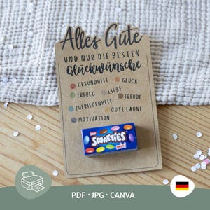 Pode incluir: Um cartão castanho com texto alemão, incluindo "Alles Gute" e "Glückwünsche", com uma caixa de mini Smarties. O cartão tem pontos coloridos com palavras alemãs. Sobre uma superfície branca texturizada.