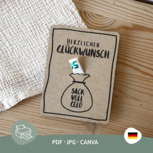 Puede incluir: Una tarjeta de papel kraft con el texto alemán "HERZLICHEN GLÜCKWUNSCH" y un dibujo de una bolsa de dinero con el texto "SACK VOLL GELD". Un billete de euro doblado está insertado en la bolsa. La tarjeta está sobre una superficie de madera.