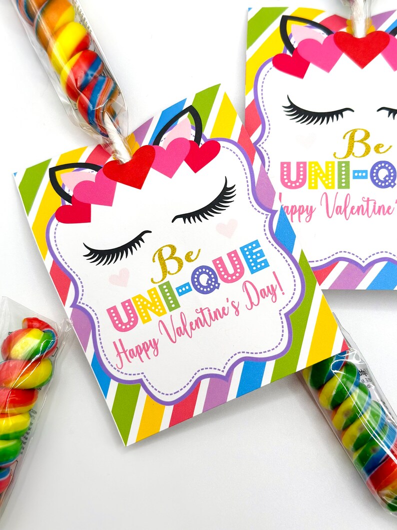 Puede incluir: Una tarjeta de San Valent&iacute;n colorida con tem&aacute;tica de unicornio con el texto "Be Unique! Happy Valentine's Day!" La tarjeta est&aacute; unida a una piruleta con caramelos de colores arco&iacute;ris.