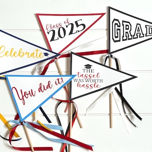 May include: Five graduation party pennant flags with different sayings. The flags are white with black and red lettering. The sayings are "Celebrate", "Class of 2025", "Grad", "You did it!" and "The tassel was worth the hassle".