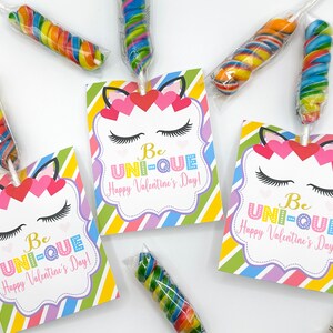 Puede incluir: Tres etiquetas de regalo de San Valent&iacute;n de unicornio coloridas con el texto "Be UNI-QUE Happy Valentine's Day!" Cada etiqueta est&aacute; decorada con una cara de unicornio, pesta&ntilde;as y corazones. Las etiquetas est&aacute;n unidas a piruletas de espiral de colores.