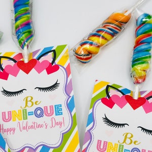 Puede incluir: Un conjunto de dos tarjetas de San Valent&iacute;n con un unicornio con rayas de colores y el texto "Be UNI-QUE Happy Valentine's Day!" Cada tarjeta viene con una piruleta colorida.