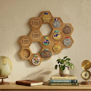 Peut inclure: Présentoir à médailles en bois en forme d'hexagone, avec des fentes pour les médailles et un motif en nid d'abeille. Le présentoir contient diverses médailles, dont celles de l'UTMB et du Marathon de Tokyo. Il est monté sur un mur beige, avec un globe, des livres et une boussole.