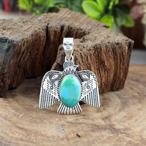 May include: A silver bird pendant with a turquoise stone. The pendant features detailed etched patterns on the wings and body. The oval turquoise stone is a vibrant blue-green colour. The pendant is designed to be worn as jewellery.