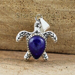 Può includere: Un ciondolo a forma di tartaruga in argento con una pietra di lapislazzuli blu intenso a forma di goccia al centro del guscio. La lavorazione del metallo presenta dettagliati motivi incisi sulla testa e sulle pinne. Il testo StarSilverIndia è visibile sopra.