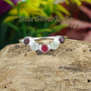 May include: A silver ring featuring five round, prong-set gemstones arranged in a curved arc. The stones alternate between deep red and pale green colors. The text StarSilverIndia is visible in the upper portion of the image above the ring.