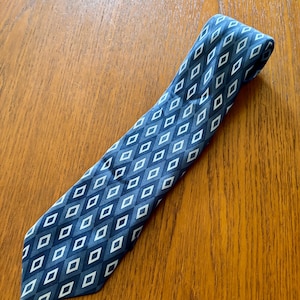 May include: A blue tie featuring a diamond pattern in shades of blue and white. The tie is displayed on a wooden surface.