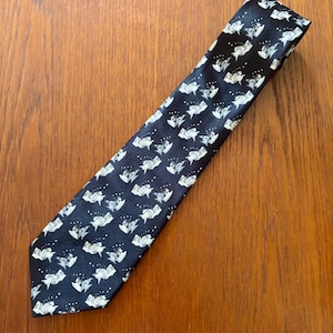 May include: A black necktie featuring a repeating pattern of small white fish illustrations. The fish are depicted in a stylised manner, swimming in various directions across the fabric, accompanied by tiny white dots representing bubbles.
