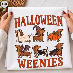 Puede incluir: Una camiseta blanca con el texto naranja HALLOWEEN WEENIES y una ilustración colorida de estilo caricatura de seis perros salchicha disfrazados de fantasma, bruja, calabaza, murciélago, esqueleto y vampiro, estampados en la prenda.