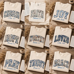 May include: A collection of nine cream-colored crewneck sweatshirts, each featuring a unique word in a collegiate font with a blue and white floral pattern. The words include CHOSEN, FAITH, JOY, HOPE, WORTHY, LOVED, PRAY, TRUST, and GRACE, with corresponding Bible verse references printed below each word.