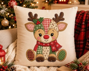 May include: A square throw pillow with an off-white fabric base featuring a central applique of a seated reindeer. The reindeer is constructed from various fabric patches in red, green, and tan, wearing a red scarf with white snowflake patterns.