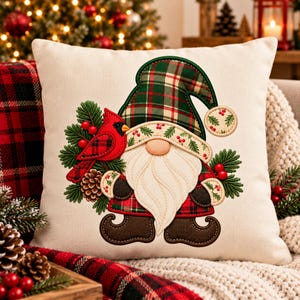 May include: A square off-white throw pillow featuring an embroidered gnome wearing a green and red plaid hat. The gnome has a white beard, brown boots, and is surrounded by green pine branches, red berries, a pinecone, and a red cardinal.
