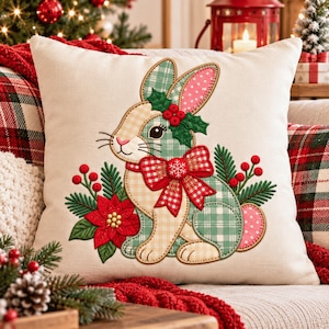 May include: A square off-white throw pillow featuring an embroidered rabbit with a green and beige plaid pattern. The rabbit is adorned with a red and white checkered bow, holly leaves, red berries, and a red poinsettia flower at its base.