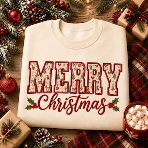May include: A cream-colored crewneck sweatshirt featuring the text MERRY in large block letters with a patterned fill of small Christmas trees and hearts, and the word Christmas in red cursive script with holly and berry accents.