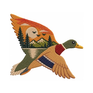 May include: An embroidered patch shaped like a flying mallard duck. The duck's wing features a landscape scene with a bright orange sunset, a pale yellow sun, dark green pine trees, snow-capped mountains, and a lake with a reflection.
