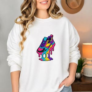 May include: White sweatshirt with a vibrant graphic of a melting trainer. The trainer design features pink, blue, yellow, and purple hues, with black detailing. The graphic has a dripping effect.