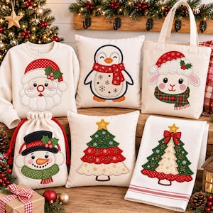 Puede incluir: Una colección de artículos textiles de color crema con diseños navideños bordados: una sudadera con Santa, una bolsa de tela con una oveja, una bolsa con cordón con un muñeco de nieve, dos cojines cuadrados y una toalla doblada con un árbol.