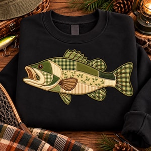 May include: A black crewneck sweatshirt featuring a large, central applique of a fish. The fish is constructed from various fabric patches in shades of green, beige, and brown, showcasing a mix of gingham, striped, and floral patterns.