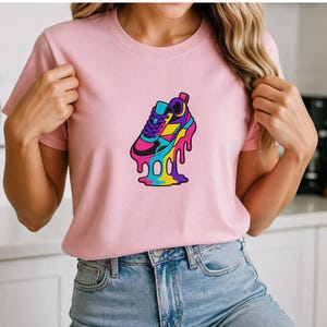 May include: A pale pink t-shirt with a vibrant graphic of a melting sneaker. The sneaker design incorporates blue, pink, yellow, and purple hues. The t-shirt is made of a soft fabric and has short sleeves.