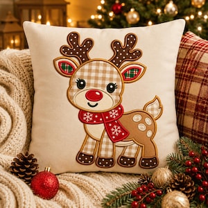 May include: A square off-white throw pillow featuring an embroidered reindeer with a tan and white checkered pattern on its head and legs. The reindeer wears a red scarf with white snowflake patterns and has a bright red nose and brown antlers.
