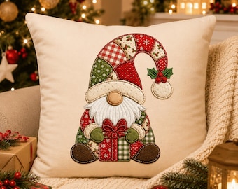 May include: A square cream-colored throw pillow featuring a central embroidered gnome design. The gnome wears a patchwork hat in red, green, and white patterns, has a white beard, and holds a red and green gift box with a bow.