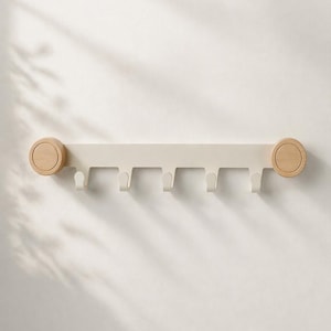 May include: A cream-coloured wall-mounted coat rack with five hooks. The rack has wooden circular end pieces and is mounted on a white wall. The hooks are evenly spaced along the bottom of the rack.