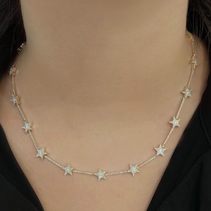 May include: A delicate gold necklace featuring a series of star-shaped pendants, each encrusted with small, sparkling gemstones. The necklace is worn around the neck, showcasing its elegant design and intricate details. The necklace is a beautiful piece of jewelry.