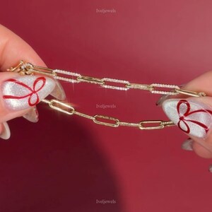 May include: Two gold link chain bracelets, one with sparkling stones, held against a red background. The bracelets are displayed by hands with festive nail art. The brand name "Iveljewels" is visible.